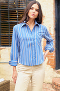Woman wearing a blue striped shirt and beige pants standing outdoors.