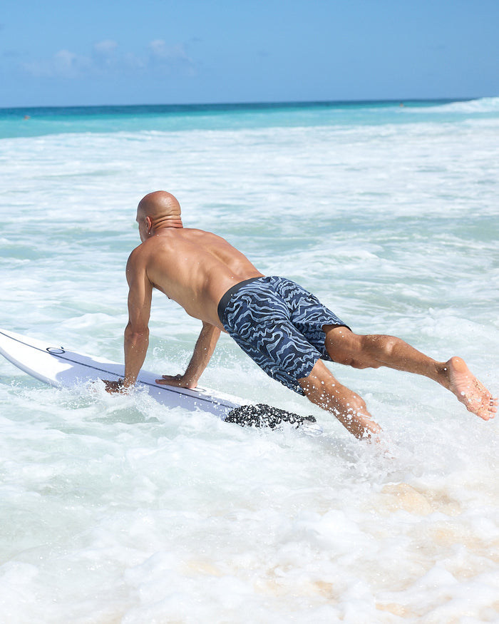 Kelly Slater wearing boardshorts with a geometric pattern in shades of blue and light blue, featuring a drawstring waistband.