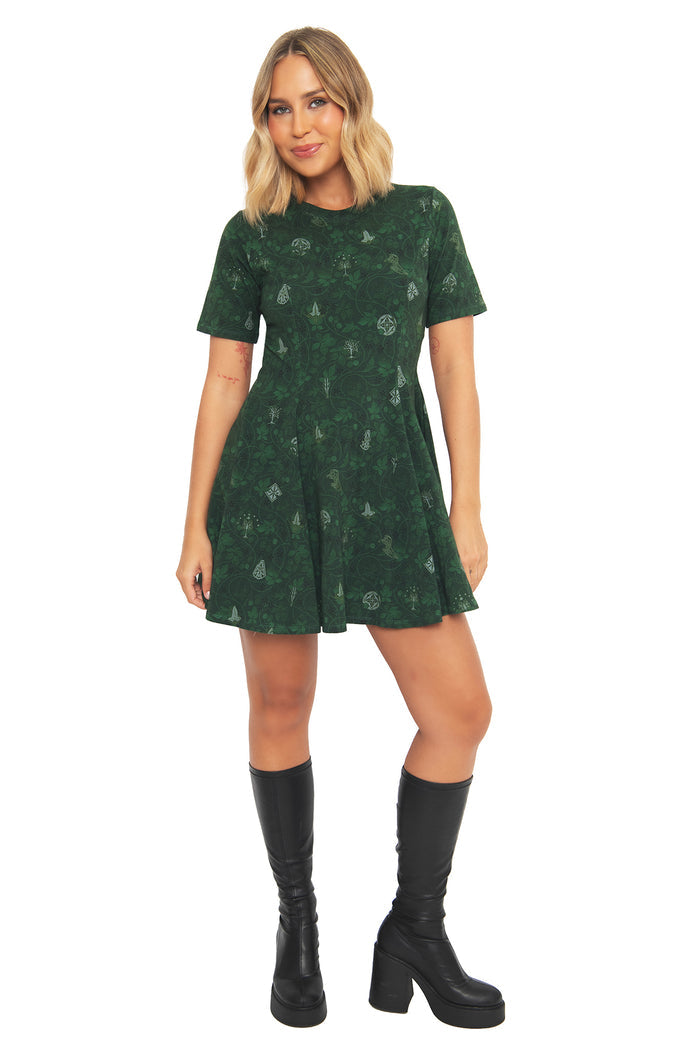 Front view of a model wearing the BlackMilk Bag End Wallpaper Evil Tee Dress, a deep green skater dress inspired by the cosy interiors of Bag End from the Lord of the Rings.