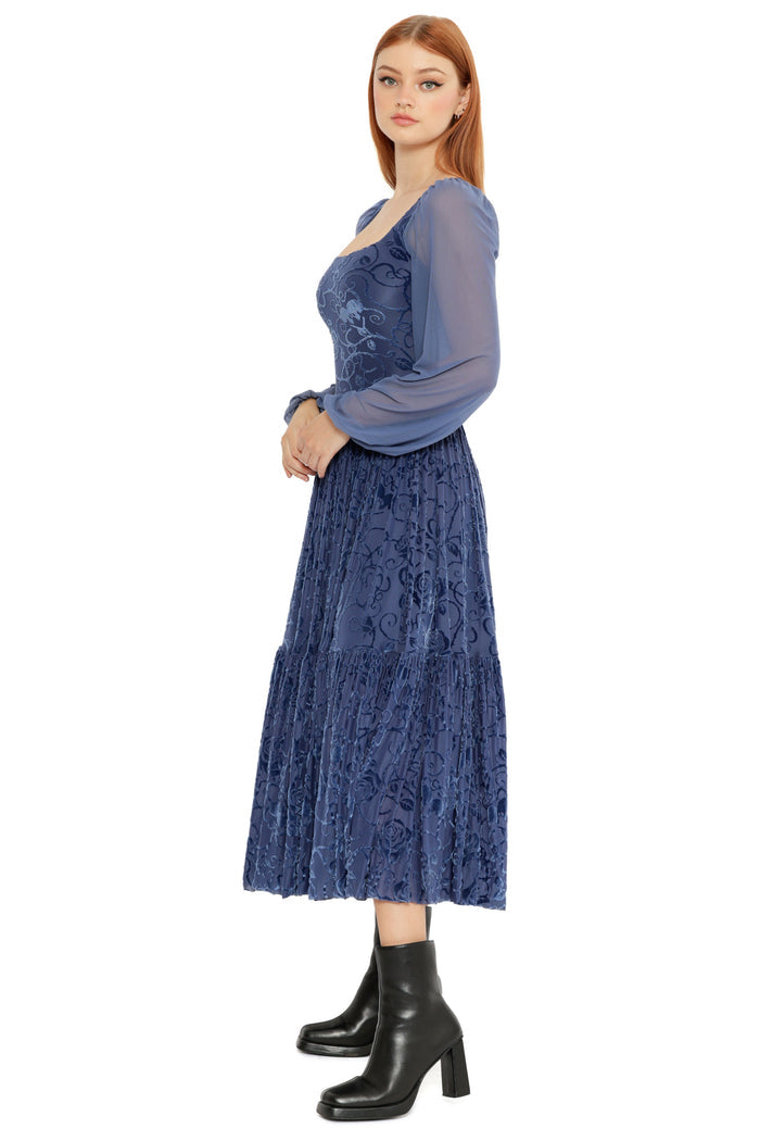 Model styled in the Be With Me Always Slate Burned Velvet Fae Queen Dress, highlighting the sheer long sleeves, square neckline and textured velvet floral fabric in a romantic midi silhouette