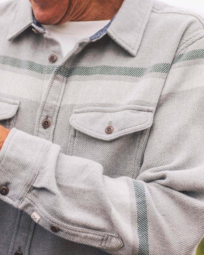 Close-up of a person wearing a light gray denim jacket with green plaid accents.