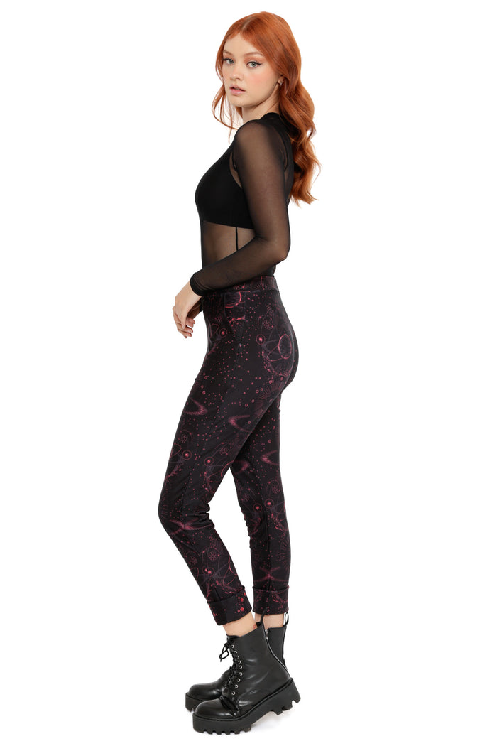 Galaxy-themed cuffed pants featuring celestial symbols, orbiting planets and deep red space print on black fabric