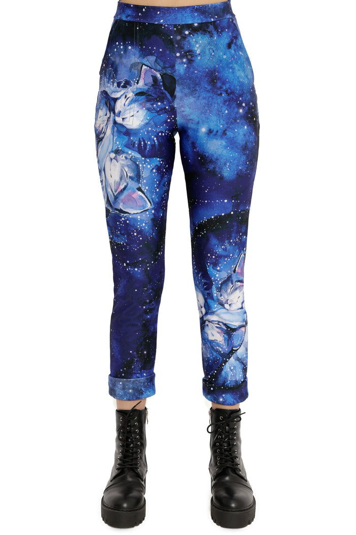 Blue galaxy-themed pants with cat designs worn by a person on a white background