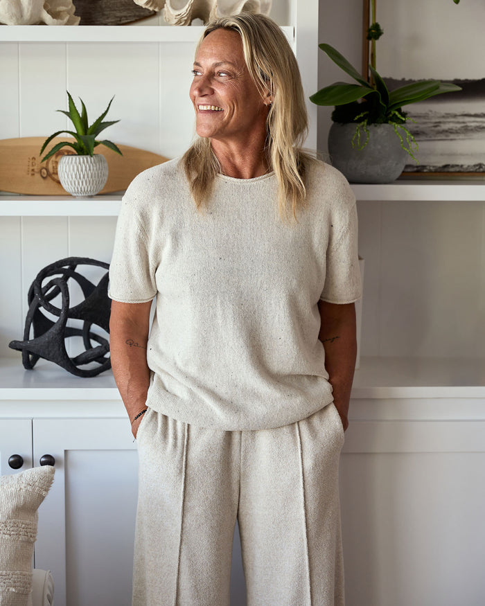 Woman wearing a beige outfit standing in a room with white walls and decorative items.