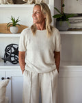 Woman wearing a beige outfit standing in a room with white walls and decorative items.