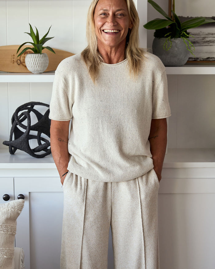 Woman wearing a beige outfit standing in a room with decorative items.