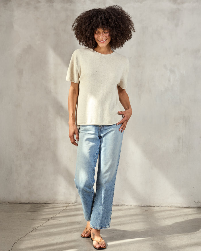 Woman wearing cream woven t-shirt with blue jeans on a neutral background