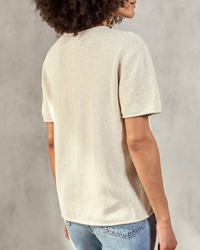 Woman wearing cream woven t-shirt with blue jeans on a neutral background