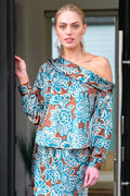 A model wearing the Finley Dani blouse, a long sleeve asymmetric satin off-shoulder top with a brown and turquoise floral print.