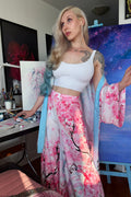 Woman in a white top and pink floral kimono standing in a room with a desk and artworks.