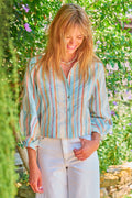 Woman wearing a striped shirt and white pants standing in a garden.
