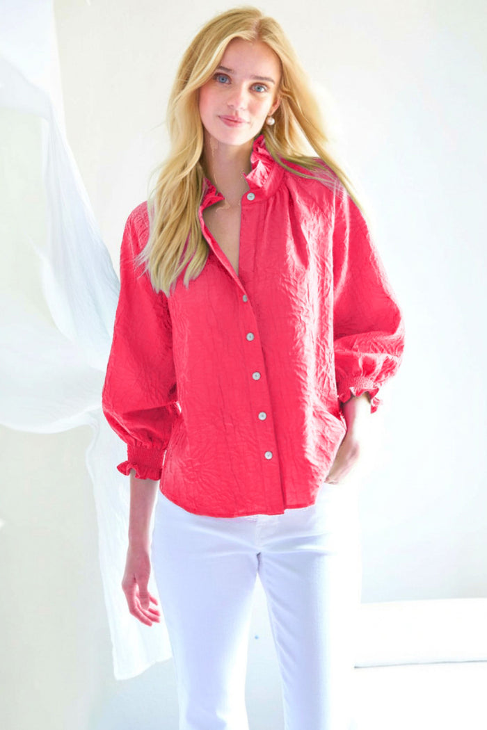Woman wearing a red button-up shirt and white pants against a white background