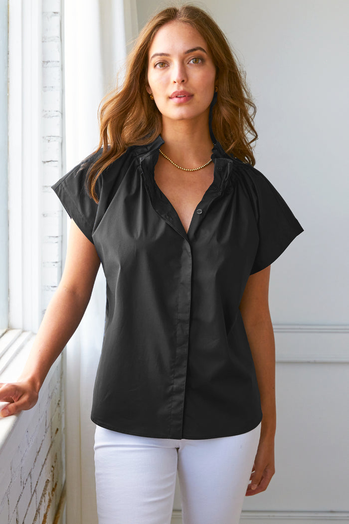 Model wears Finley Jenny black silky poplin top with ruched ruffle detail and stand collar.