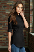 Woman wearing a black shirt and blue jeans against a brick wall.