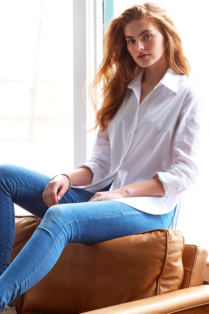 A model wearing the Finley Keller blouse, a casual white poplin button-down shirt with a high shirttail and a relaxed fit.