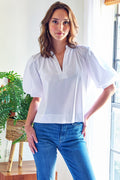 Woman wearing a white blouse and blue jeans standing indoors with plants in the background