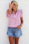 Woman wearing a red and orange striped ruffle accent shirt against a white brick wall.