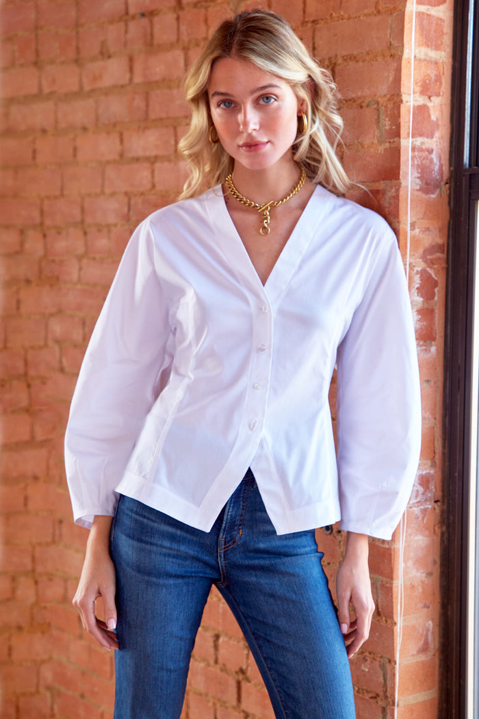 Woman wearing a white blouse and blue jeans standing against a brick wall.