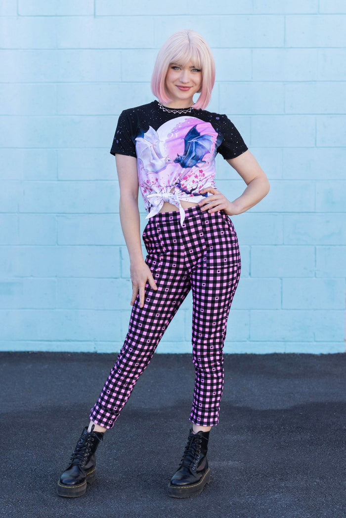 Person wearing a black t-shirt with a colorful design and purple checkered pants against a blue wall.
