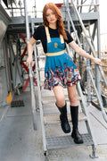 Model wearing Fallout x BlackMilk Pack Rat Apron Dress featuring Vault-Tec blue design with Fallout collectibles print at the hem.