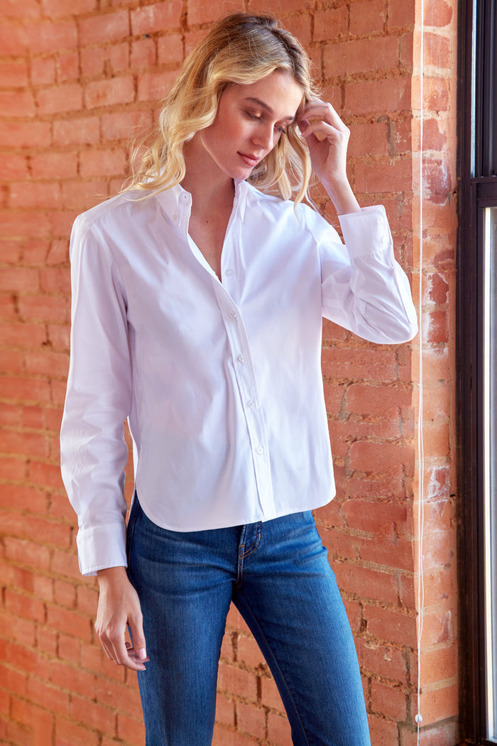 Woman wearing a white blouse and blue jeans against a brick wall.