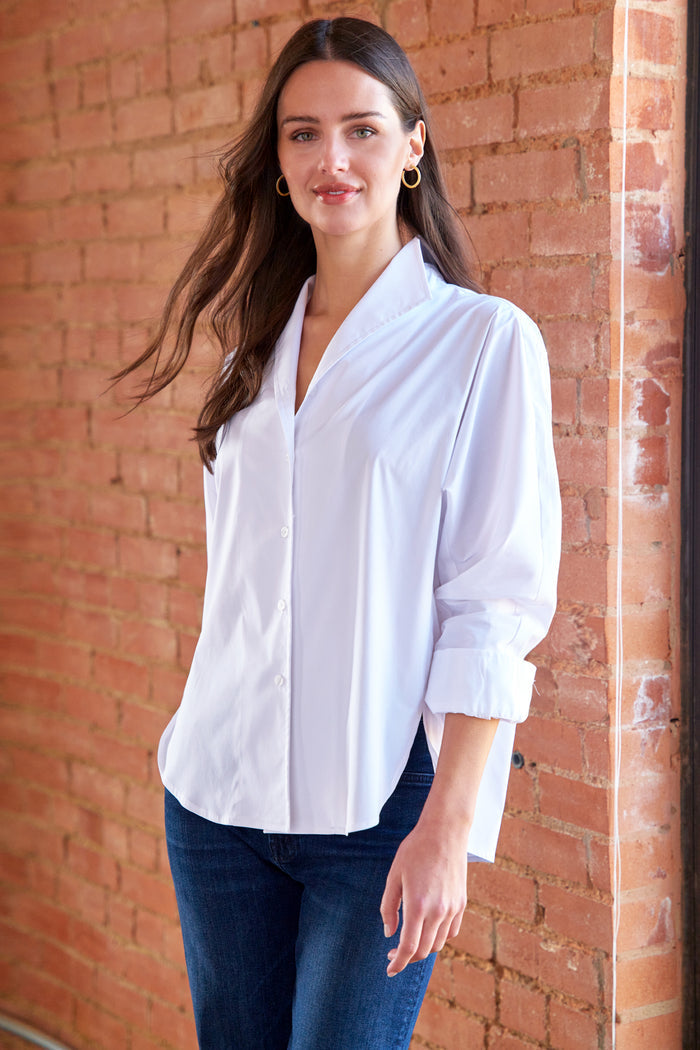 Woman wearing a white blouse and blue jeans standing against a brick wall.