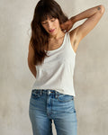 A woman wearing a white tank top and blue jeans.