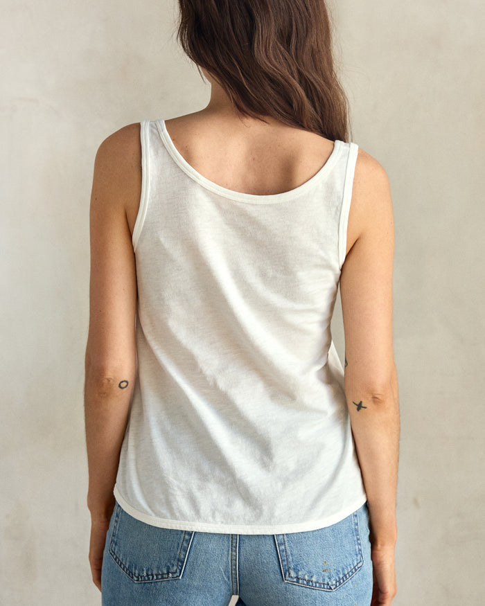A woman wearing a white tank top and blue jeans, facing the back