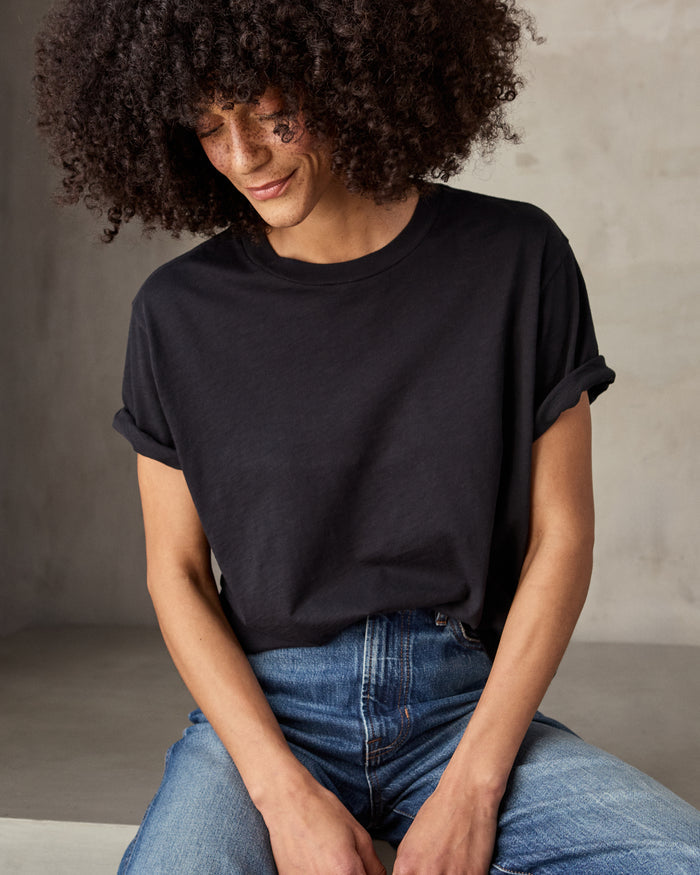A woman sitting and wearing a black short-sleeved t-shirt and blue jeans.