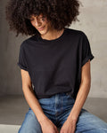 A woman sitting and wearing a black short-sleeved t-shirt and blue jeans.
