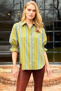 Woman wearing a green and yellow striped shirt with brown pants standing outdoors.