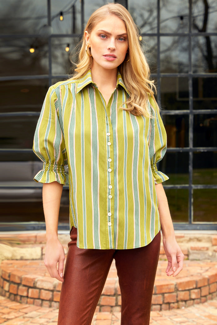Woman wearing a green and yellow striped shirt with brown pants standing outdoors.