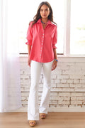 Woman wearing a coral shirt and white pants standing in a room with a brick wall.