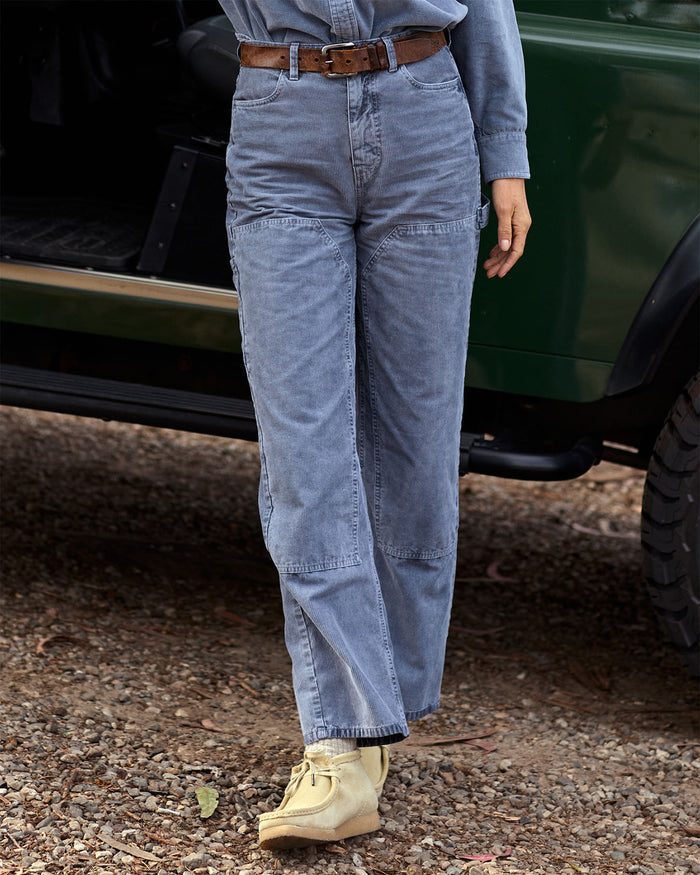 Person wearing blue pants and a brown belt standing next to a green vehicle.