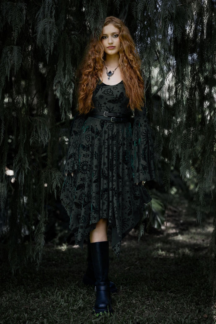 Pine green burned velvet handkerchief dress covered in witchy sigils, celestial symbols and mystical occult artwork. This whimsigoth midi dress blends dark fairycore, fantasy witch and gothic fashion aesthetics with dramatic bell sleeves and a flowing asymmetric hem.