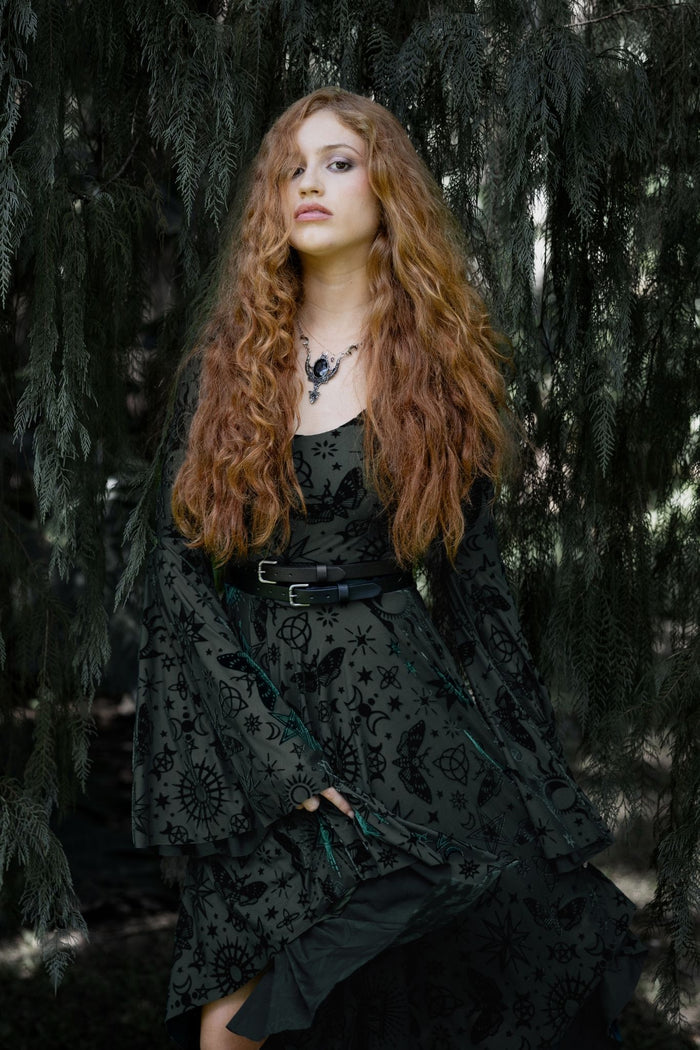 Gothic witch dress with pine green burned velvet, celestial sigils and flowing asymmetric hems inspired by nature witch aesthetics. Featuring sheer bell sleeves and a fitted bodice, this whimsigoth dress is perfect for fantasy witch and alternative goth styling.