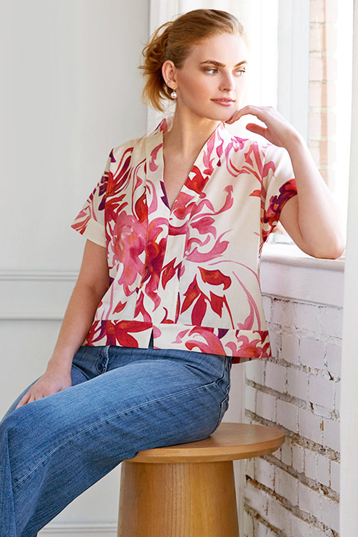 Woman wearing a floral blouse and jeans sitting on a stool indoors.