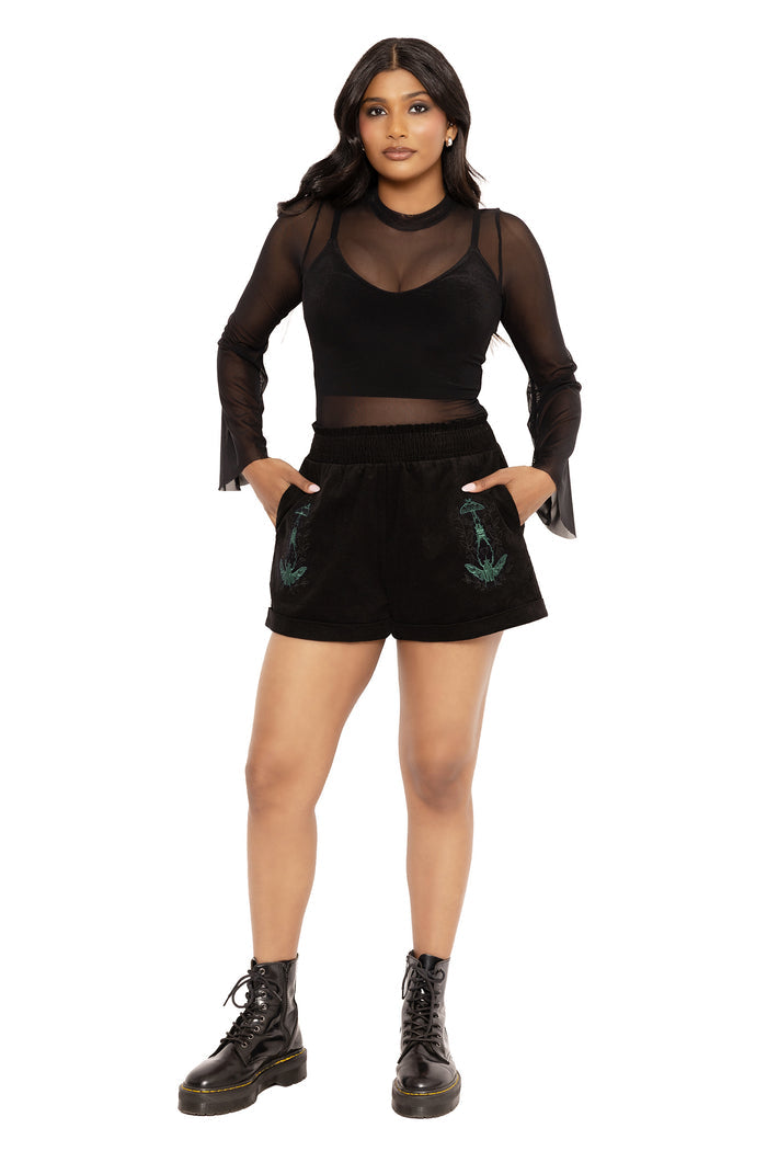 Whimsigoth black corduroy shorts with embroidered moth details by Ami Raithe, combining gothic streetwear with fantasy witch and cottagecore fashion influences. These relaxed fit paper bag shorts feature cuffed hems, pockets and soft cotton corduroy fabric perfect for alternative goth and modern witch styling.