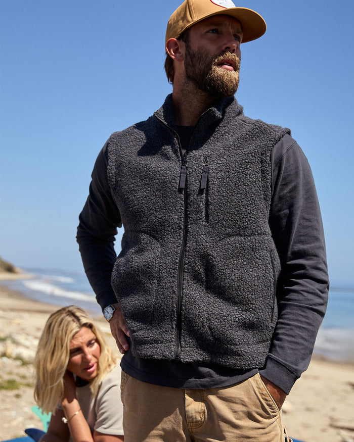 A man wearing a black wool vest on the beach
