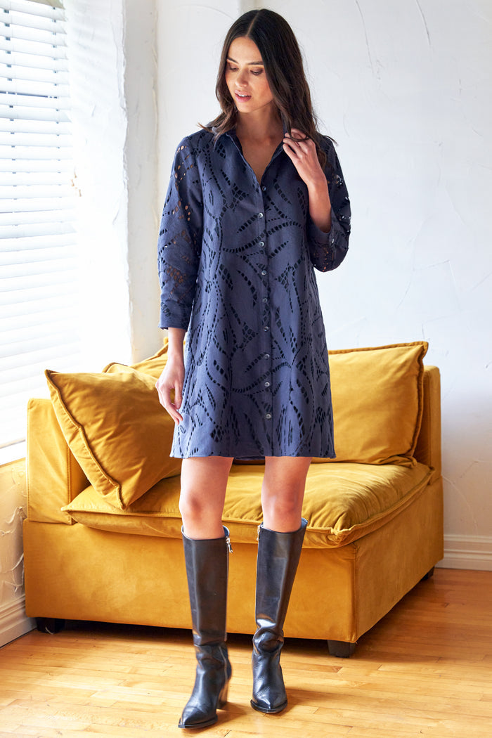 Woman wearing a blue dress and black boots standing in a room with a yellow couch.