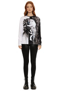 Model wearing a black and white graphic long-sleeve shirt with black pants on a white background