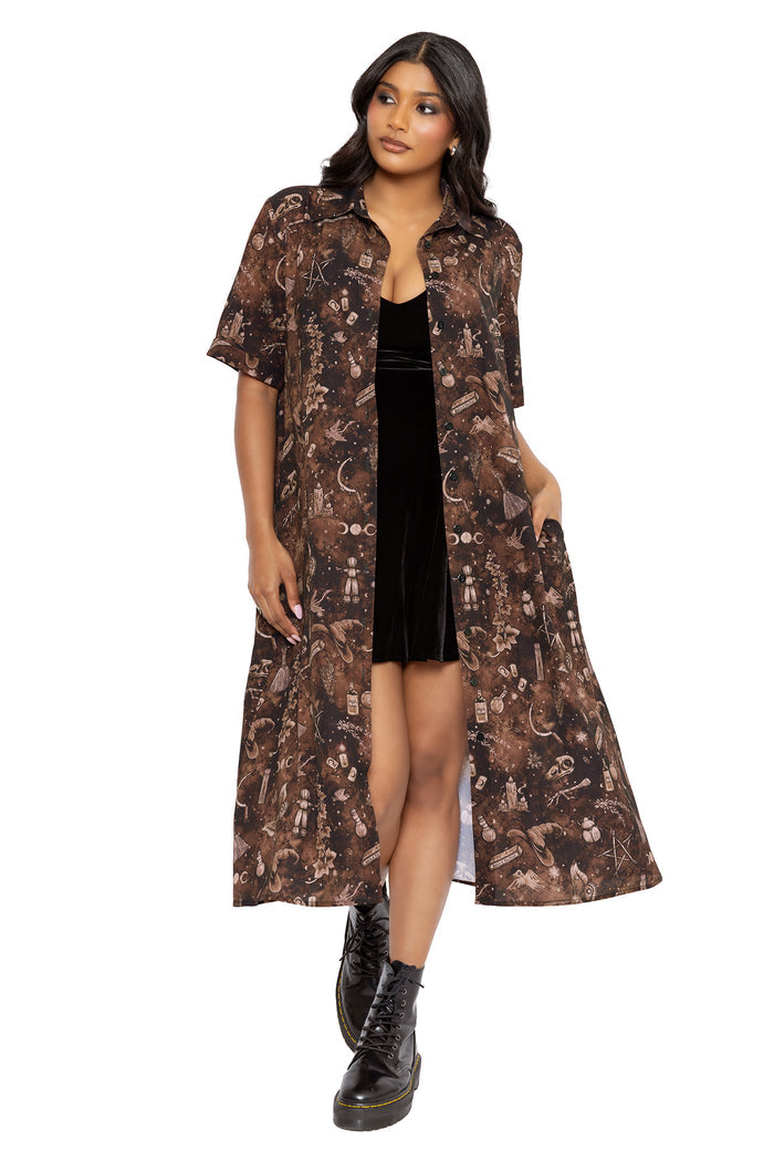 Gothic midi dress with potion bottle artwork, magical symbols and occult inspired details throughout a moody brown print by Ami Raithe. Featuring turned-back sleeves, a collared button front and flowing A-line skirt, this alternative witch dress captures dark academia fashion vibes.