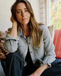 Woman sitting on a couch wearing a denim jacket with a blurred outdoor background